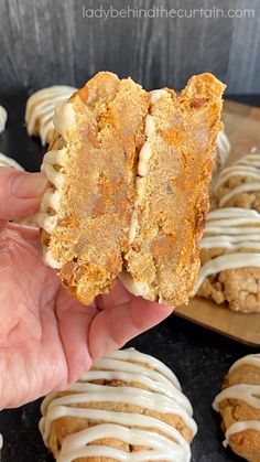 a person holding up a piece of food in front of some cookies and icing