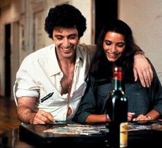 a man and woman sitting at a table with wine bottles in front of them smiling