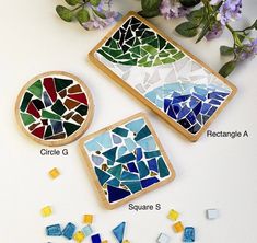 three pieces of colorful mosaic glass sitting on top of a white table next to purple flowers