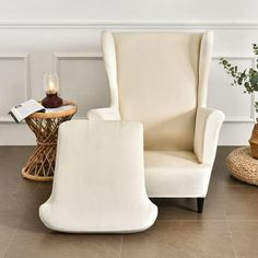 a white chair and footstool in a living room with wood flooring, wicker side table and potted plant