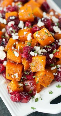 a white plate topped with sweet potatoes, cranberries and feta cheese on top