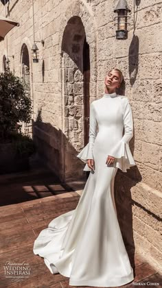 a woman in a white dress leaning against a stone wall with her hands on her hips