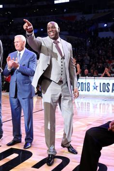 two men in suits and ties standing on a basketball court with their hands up to the crowd