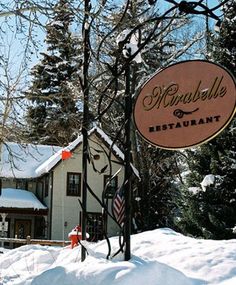 a sign for a restaurant in the middle of winter with snow on the ground and trees around it