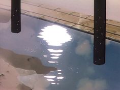 the reflection of clouds in water is seen from under an umbrella pole with two poles