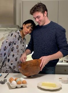 a man and woman preparing food on a kitchen counter top with eggs in bowls next to them