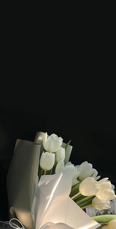 white tulips and other flowers in a vase on a black background with an envelope