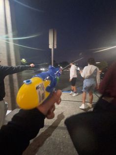 a person holding a yellow and blue object in their hand while others walk by at night