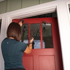 a woman is painting the front door of a house with red paint and black trim