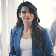 a woman in a blue jacket and white top smiles at the camera with her hands on her hips