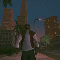 a man standing in the middle of a street at night with palm trees and tall buildings behind him