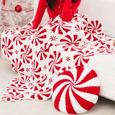 a woman is sitting on a couch with a red and white crocheted blanket