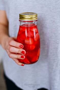 a woman holding a jar filled with red liquid and strawberries in it's hands