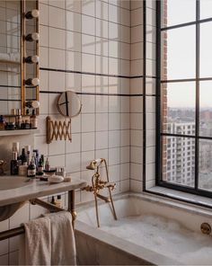 a bath tub sitting next to a window in a bathroom with white tile and gold fixtures