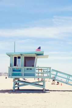 a lifeguard tower on the beach with people sitting and standing in the sand around it