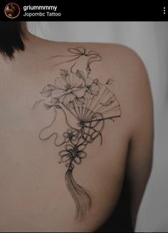 the back of a woman's shoulder with flowers and fan tattoos on her left side