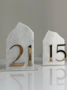 two white marble blocks with gold numbers sitting on top of each other in the shape of houses