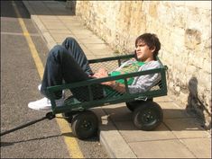 a man sitting in a green wagon on the side of a road next to a wall