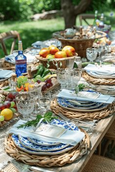 an outdoor table set with plates, glasses and fruit in baskets on top of it