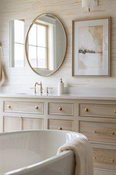 a white bath tub sitting next to a bathroom sink under a round mirror on a wall