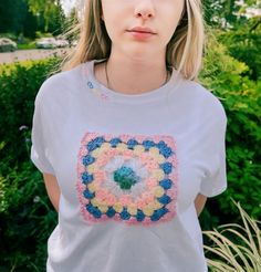 a woman wearing a white t - shirt with a crocheted square on it