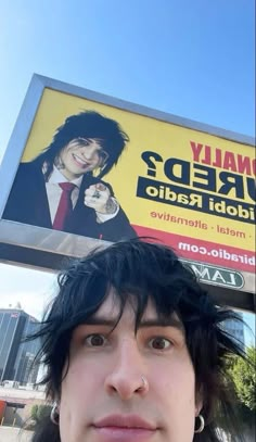 a man standing in front of a billboard with his hair pulled back to the side