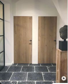 two wooden doors in an empty room with black tile flooring and white walls behind them