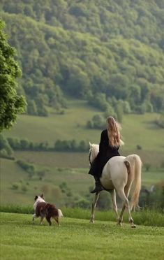 a woman riding on the back of a white horse next to a dog