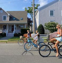 three women riding bikes down the street with surfboards on their back's rack