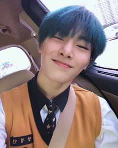 a young man with blue hair wearing a vest and tie in a car smiling at the camera