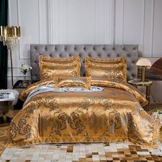 a bed with gold and silver comforters in a room next to a couch, coffee table and chandelier