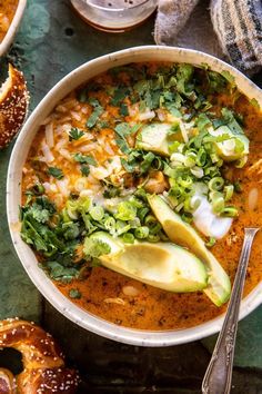 a white bowl filled with soup and topped with avocado, cilantro, bread