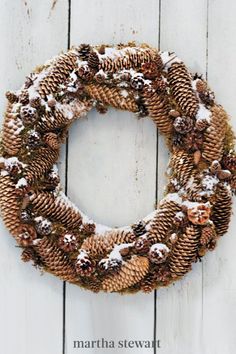 a wreath made out of pine cones covered in snow on a white wooden background with the words merry christmas written below it