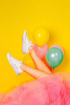 a woman in white tennis shoes and pink tulle skirt with balloons on yellow background