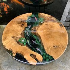 a wooden plate with fish and plants on it sitting on the ground in front of a painting