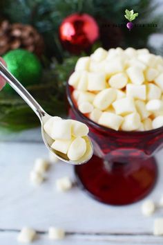 someone is spooning marshmallows out of a red glass bowl with christmas decorations in the background