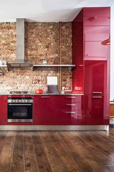 a kitchen with red cabinets and wood floors in the middle, along with a brick wall