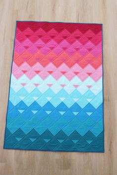 a colorful quilt is laying on top of a wooden floor in front of a wall