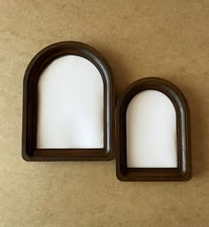 two oval wooden frames with white paper in them on a brown surface next to each other