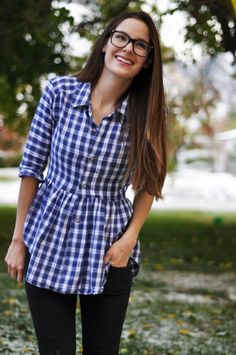 a young woman wearing glasses and a blue checkered shirt is standing in the grass