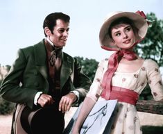 a man sitting next to a woman in a dress and hat on top of a bench