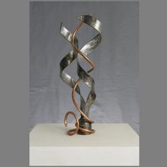 a metal sculpture sitting on top of a white table next to a gray wall in the background