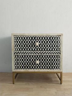 a white and black patterned chest of drawers on a wooden floor next to a wall