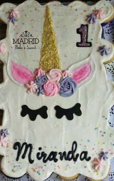 a decorated cake with an unicorn face and flowers on the top is sitting on a doily