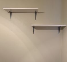 two white shelves on the wall above a toilet in a room with no one inside