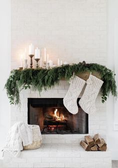 a white fireplace with stockings and candles on it, surrounded by greenery in front of the fire