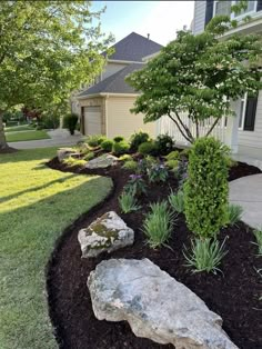 a rock in the middle of a flower bed next to a tree and grass area