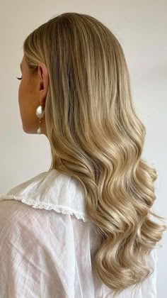 a woman with long blonde hair wearing a white blouse and pearl earrings is looking off to the side