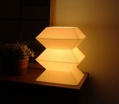 an illuminated lamp sitting on top of a wooden table next to a potted plant