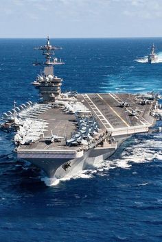 an aircraft carrier is in the middle of the ocean with other ships behind it,